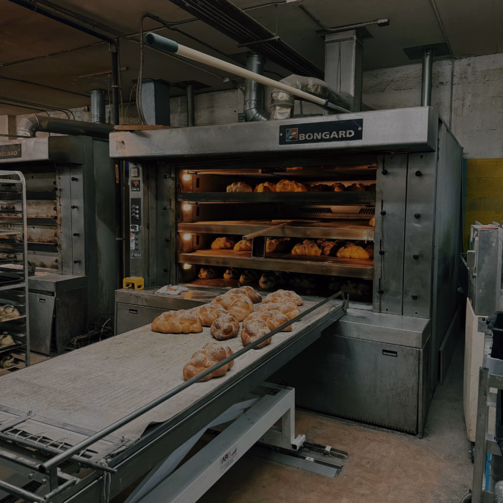 Industrie-Backofen in einer Bäckerei mit frisch gebackenen Broten auf einem Förderband – energieintensive Backproduktion mit Gewerbegas in der Bäckerei.